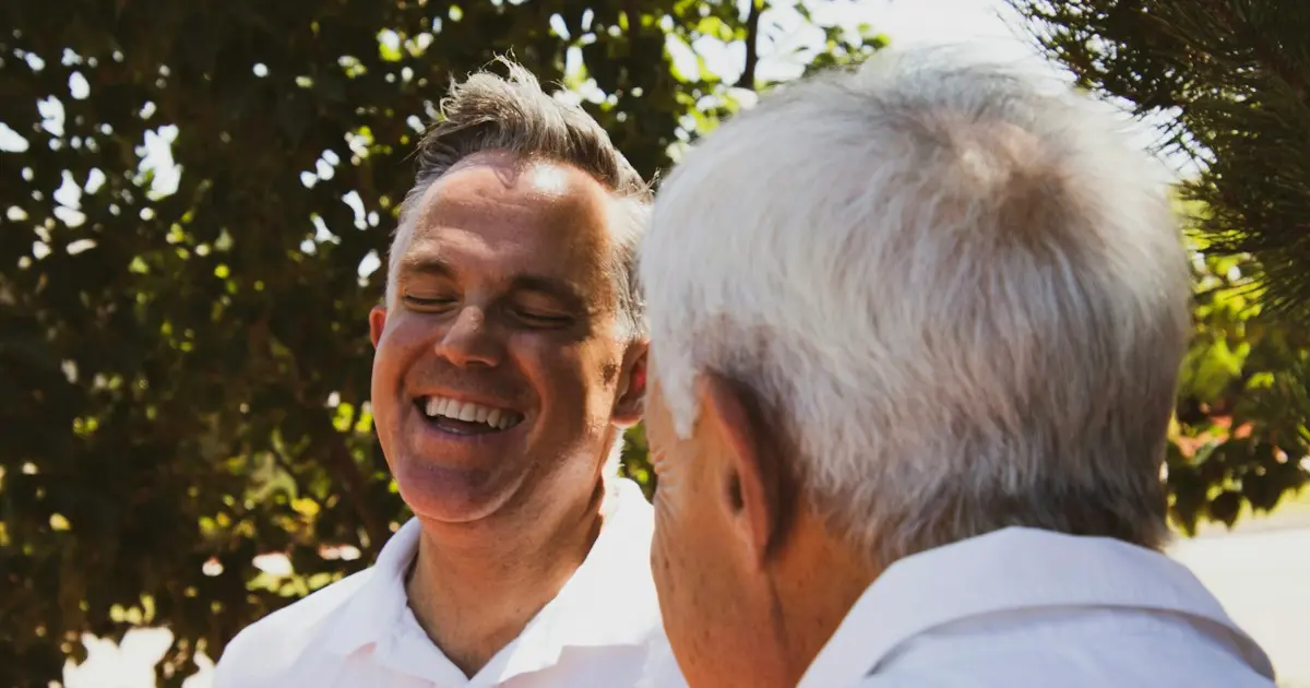 Homem conversa e ri com um senhor idoso ao ar livre