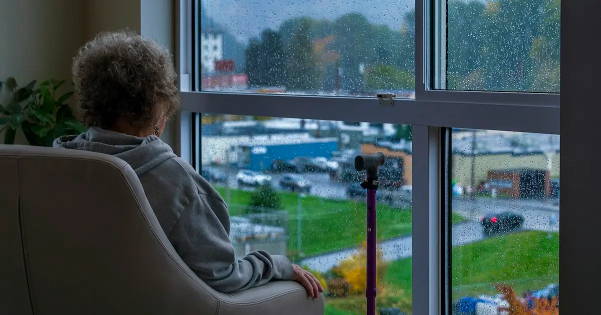 Senhora idosa sentada na poltrona olha pela janela em um dia de chuva