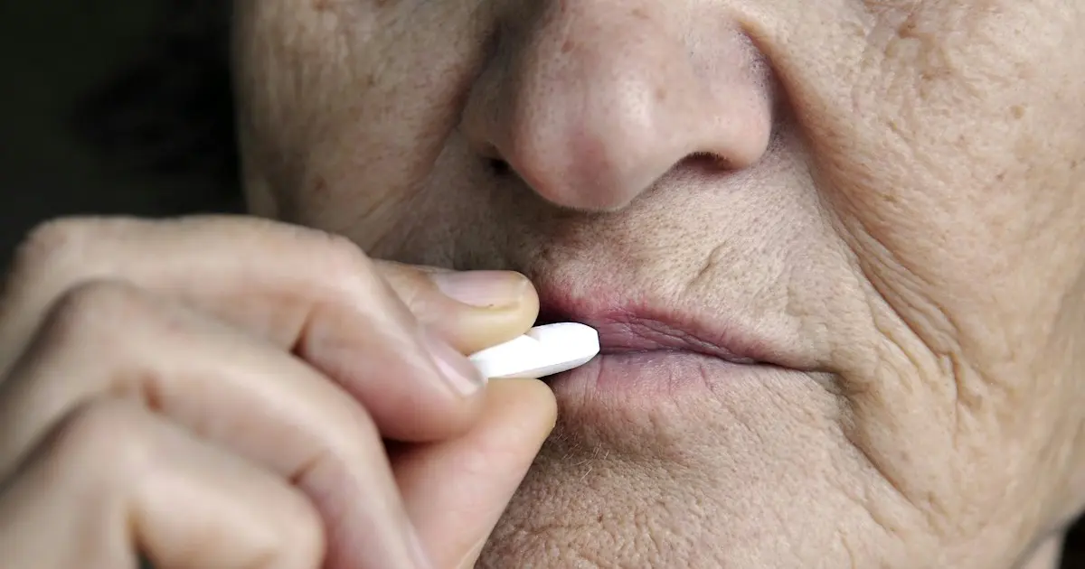 Senhora idosa colocando um comprimido branco na boca