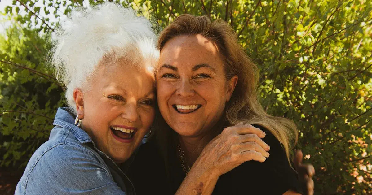Mãe idosa e filha adulta abraçadas e sorrindo ao ar livre