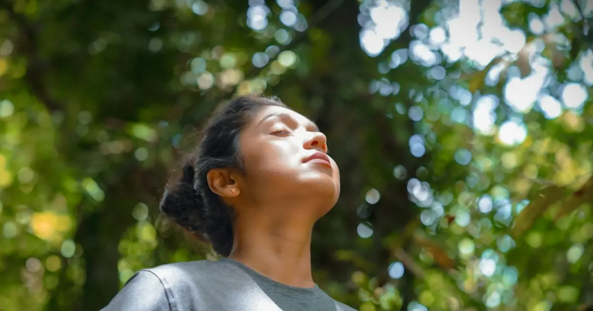 Mulher de olhos fechados respirando ao ar livre, entre árvores